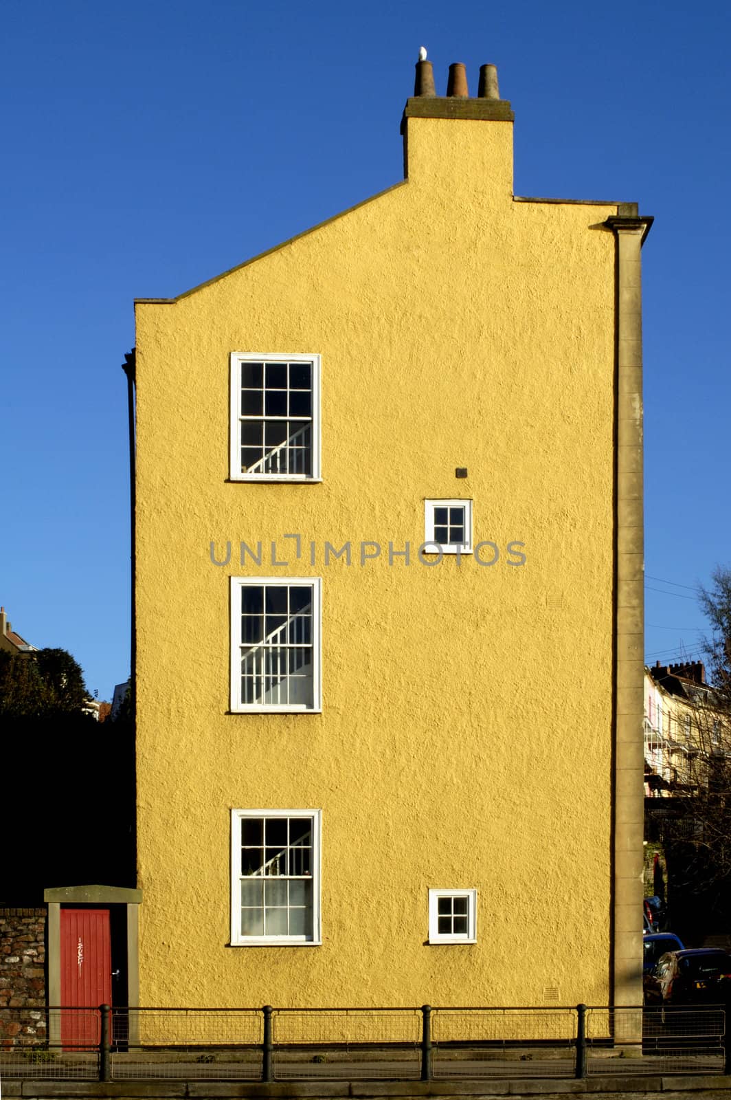 The yellow end of a line of terraced houses, against a clear blue sky. A white dove sits on one of the chimney-pots.