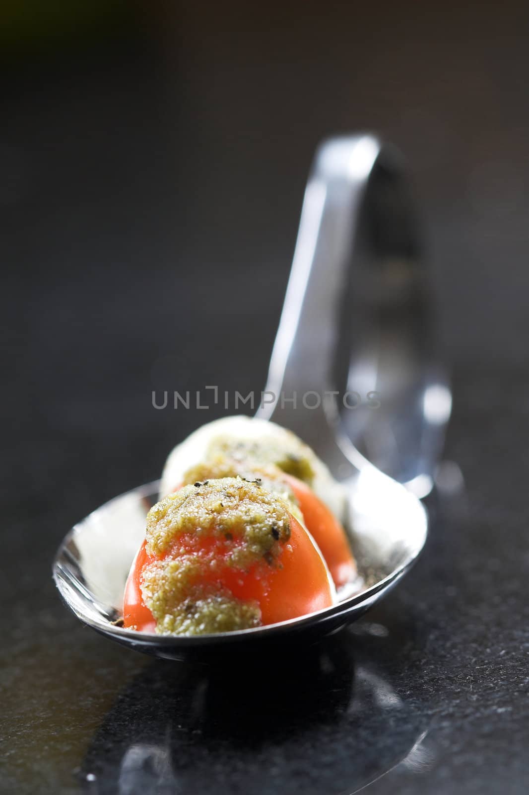 Spoon filled with amuse made of small cherry tomatoes, pesto and mozarella (shallow DOF)