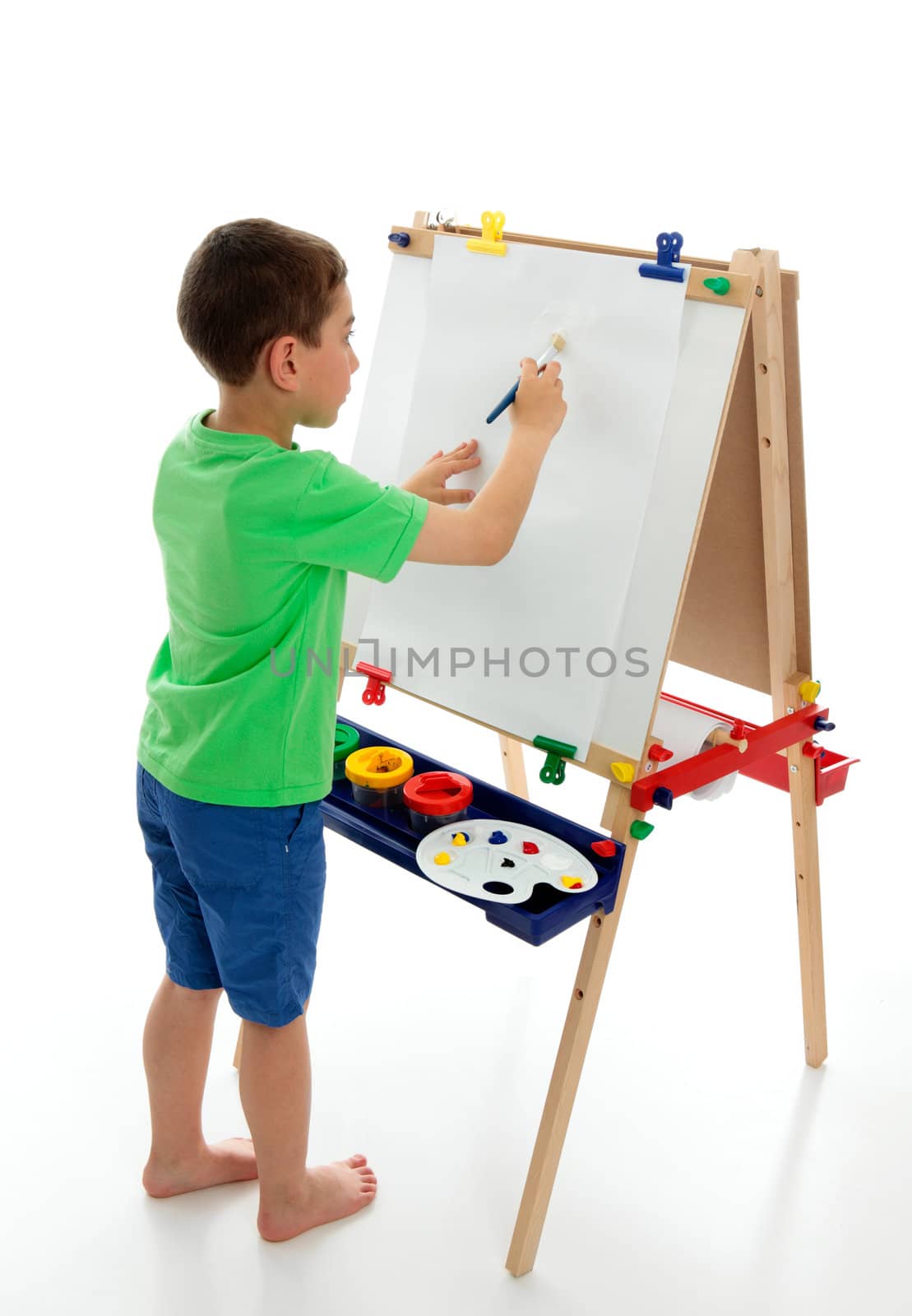 A little boy starting to paint a picture using acrylic paints and art paper on an easel.  White background.