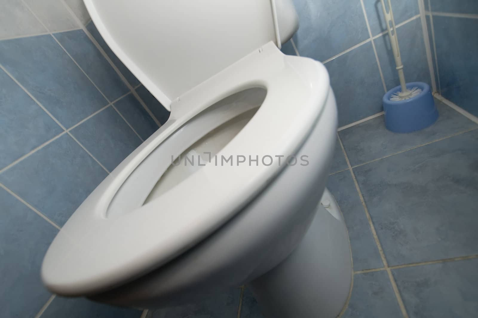 tilted white toilet detail photo, tiled floor and walls, 