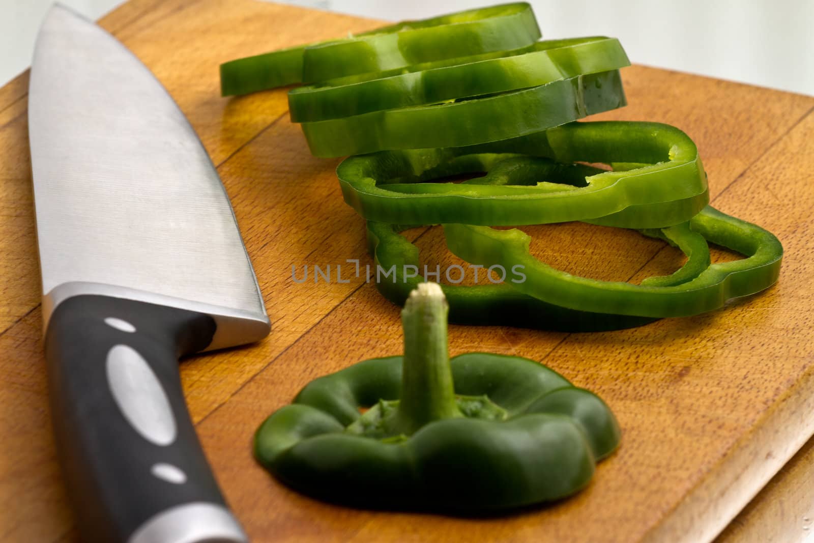 Green bell peppers being sliced at wooden cutting board with knife