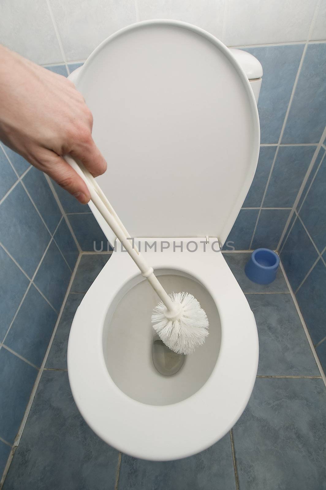human hand holding a cleaning brush before white toilet, tiled floor and walls