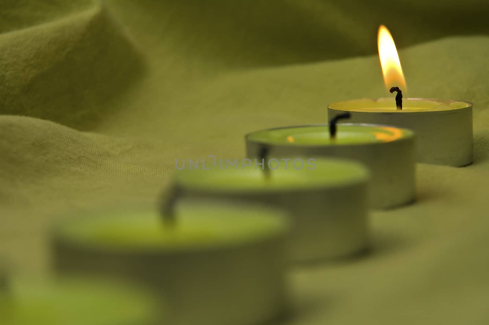dark green candles on a fabric background, only one candle is still burning