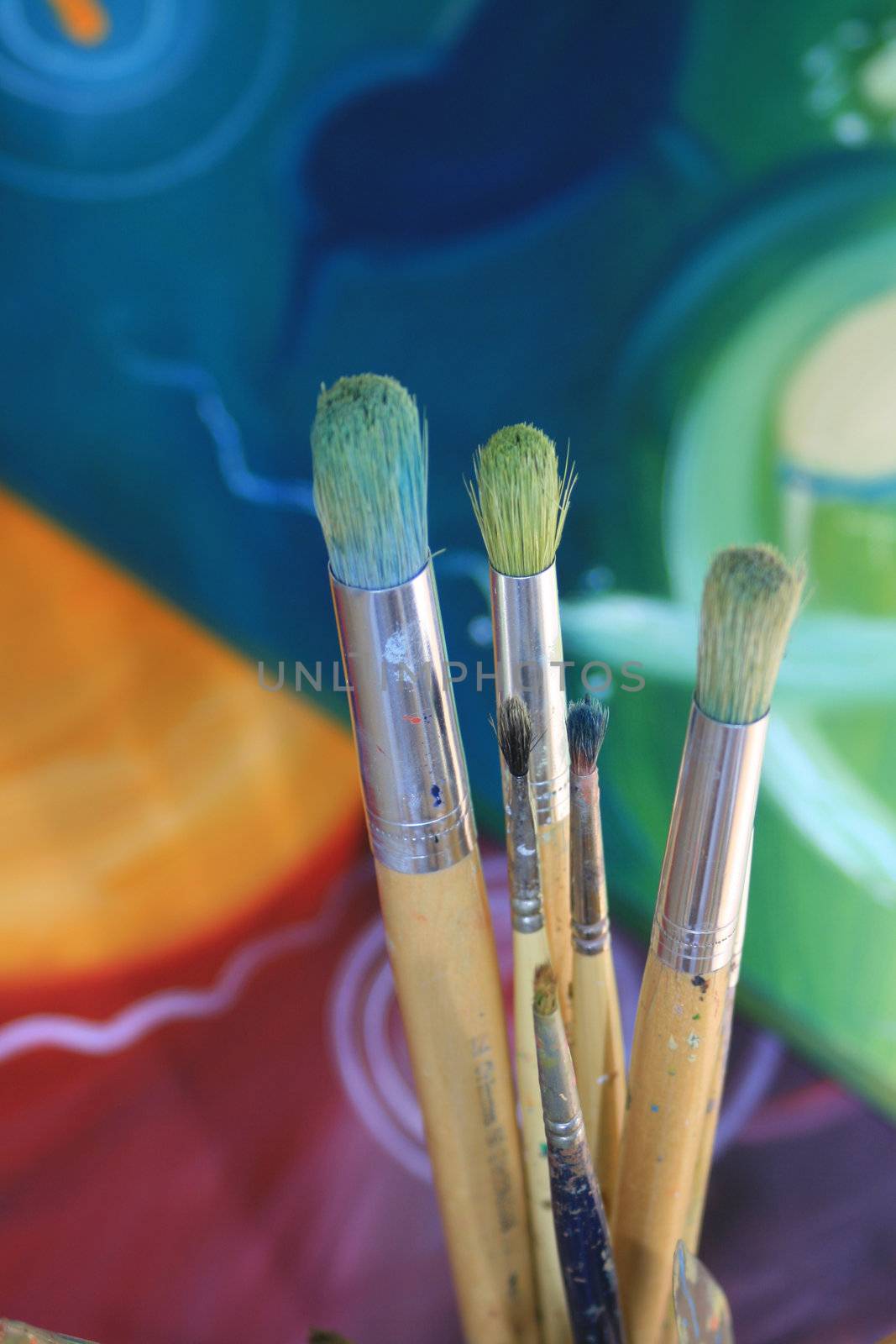 Close up detail of a set of artisist brushes with a soft focus abstract coloured painting in the background, painted by myself as the artist.