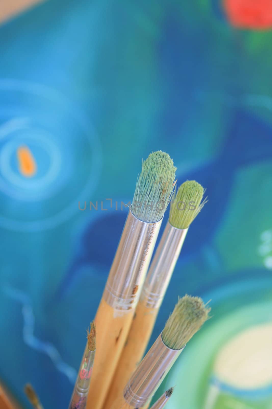 Close up detail of a set of artisist brushes with a soft focus abstract coloured painting in the background, painted by myself as the artist.