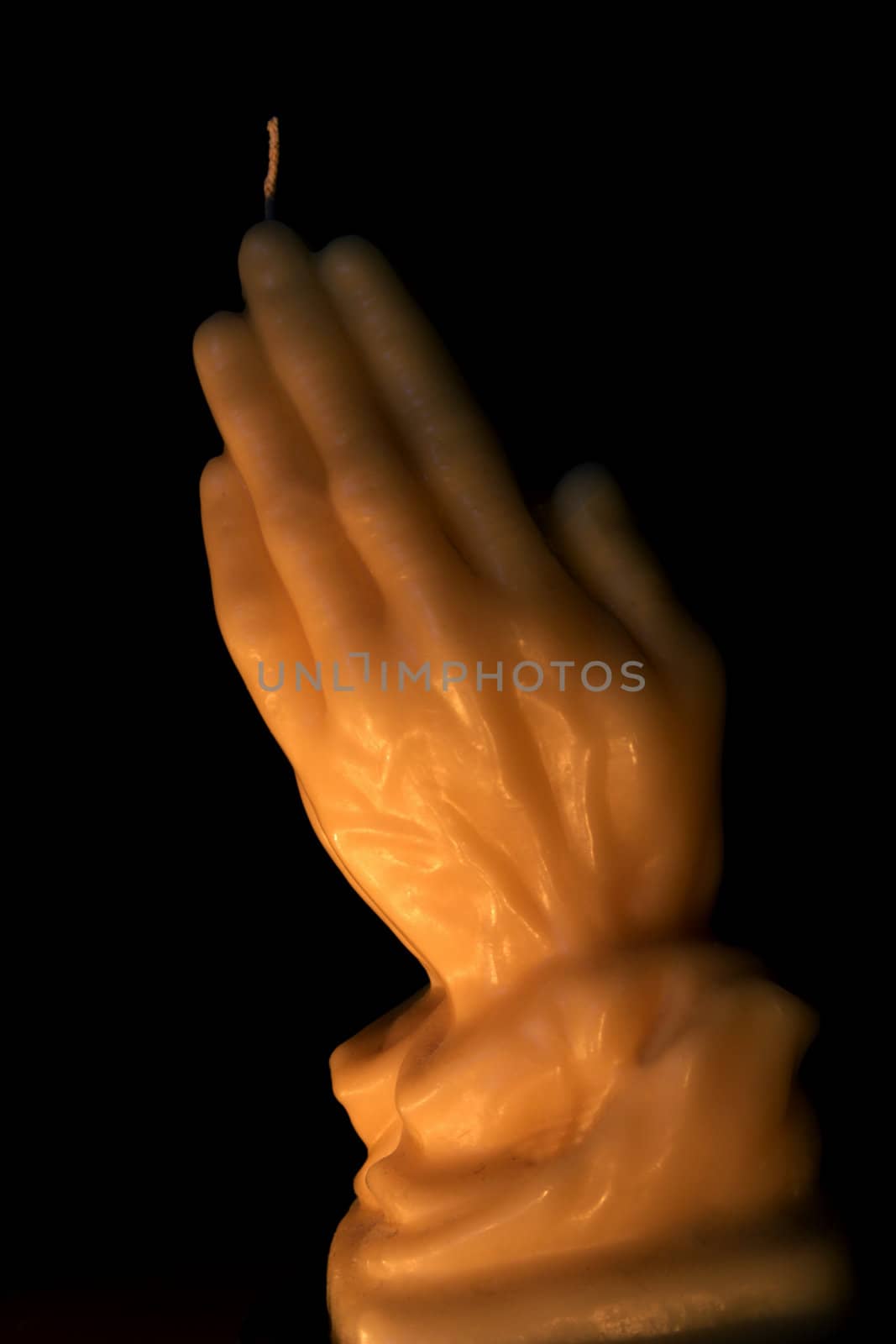 A wax candle of hands praying on black.
