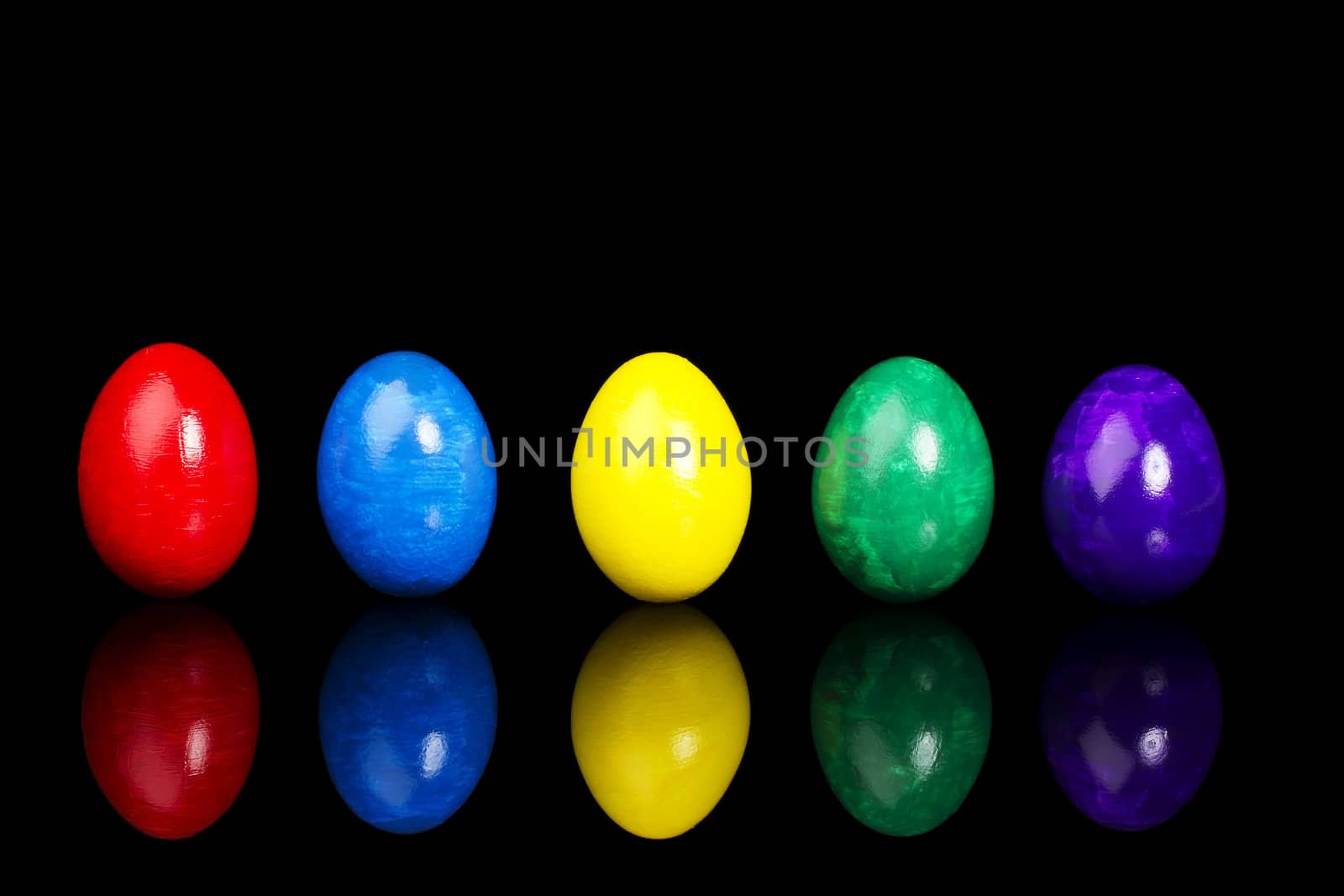row of five colorful easter eggs on black background with reflection