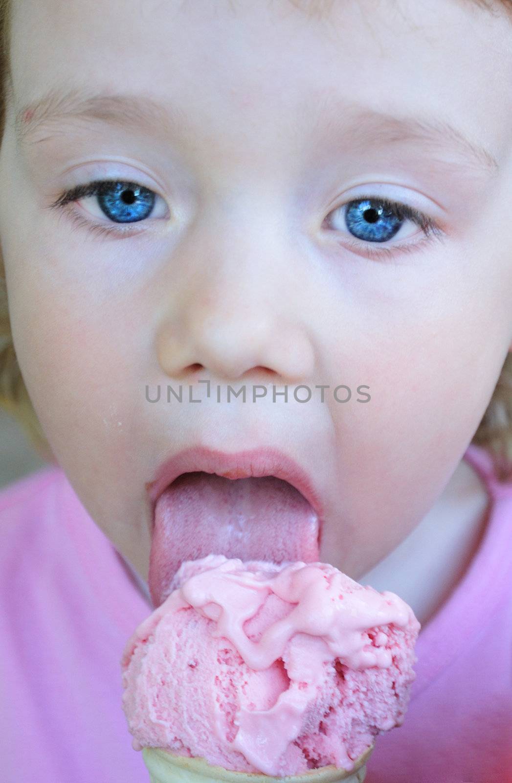 face of little pretty blue eyed girl who is eating  pink ice cream 