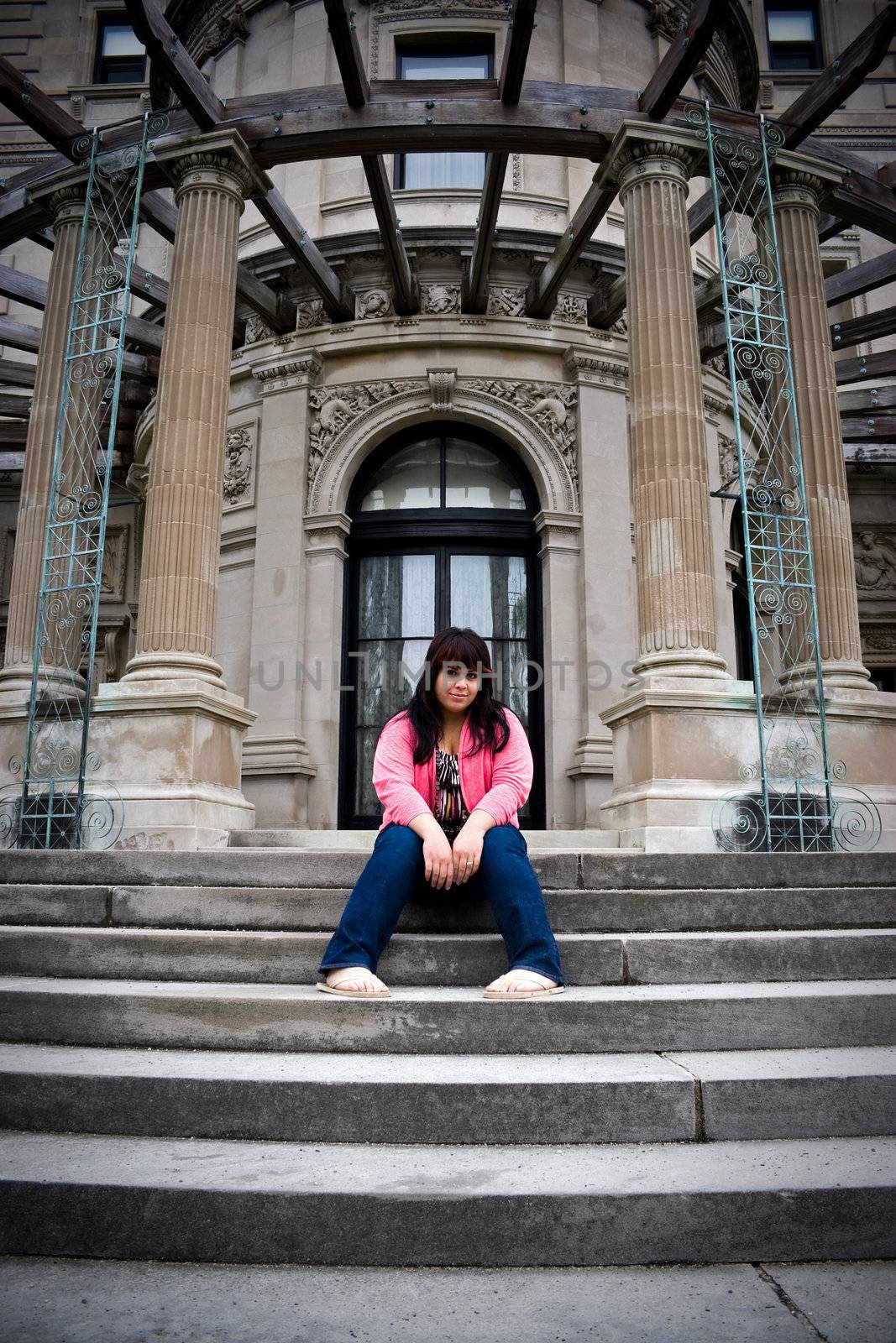 A young latin woman sitting on the steps of an old mansion.