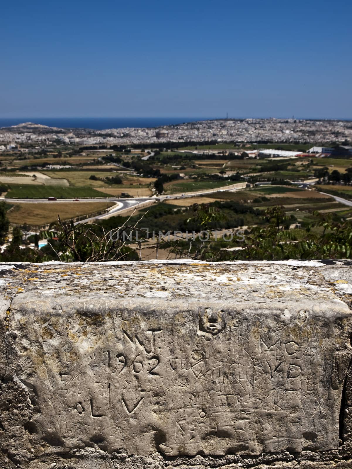 Graffiti and inscriptions on a medieval limestone wall with view of Malta in background