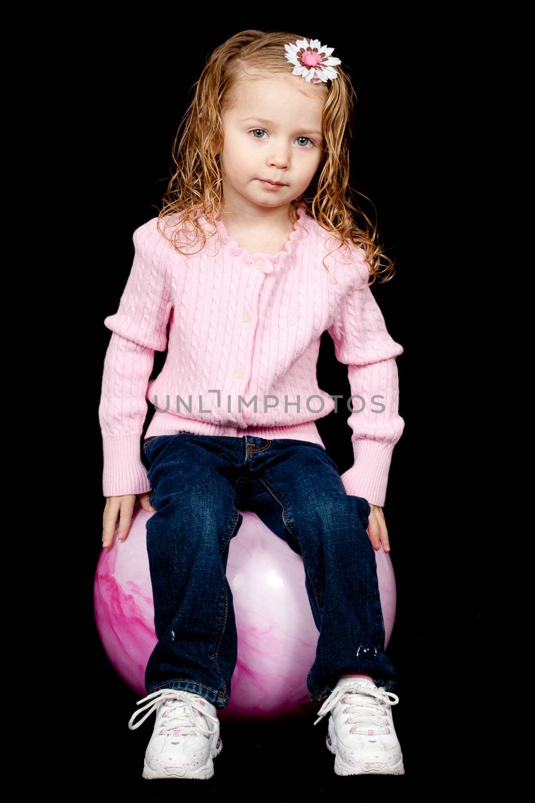 A lone content child sitting on her pink rubber ball.