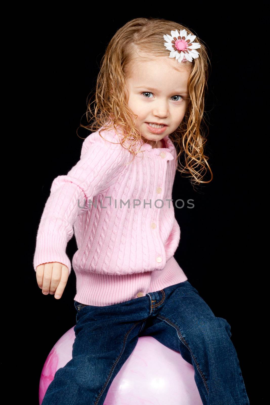 An adorable young child playing on a pink ball.