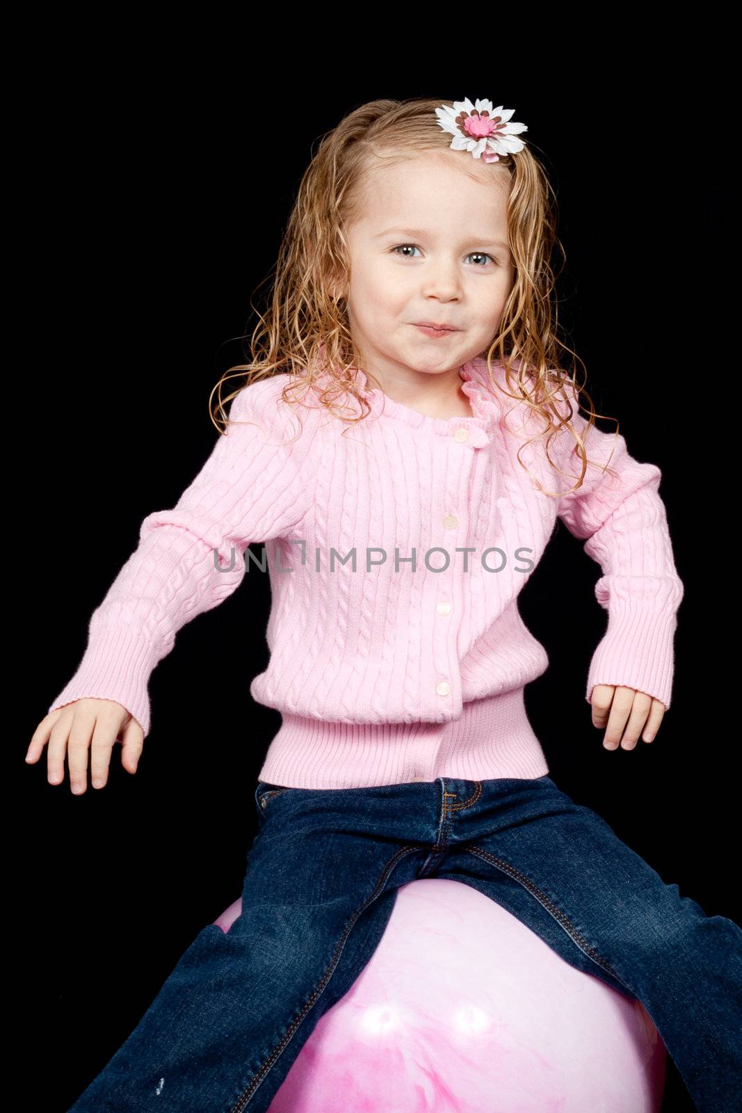 A cute child exercising on a pink ball.  She has a look of excitement and happiness on her face.