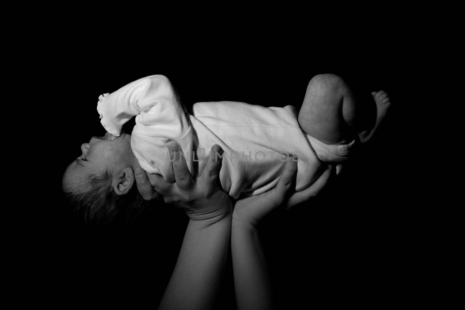 A baby being held in the air.  The child is risen above.  Image in black and white.