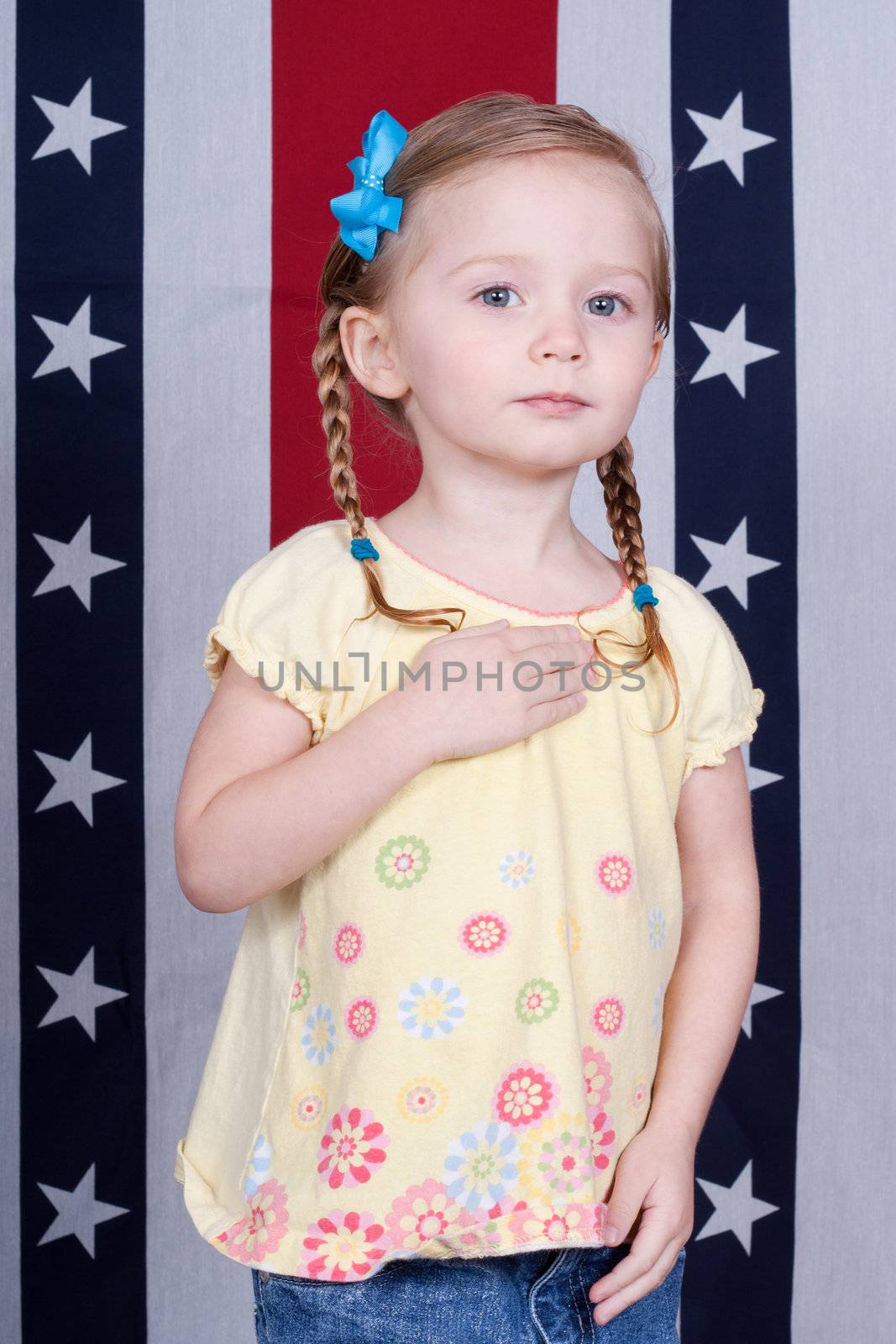 Adorable girl pledging alegiance in front of a patriotic design.