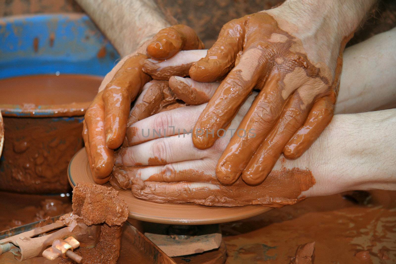 A Craftwoman's hands guiding a other hands, to teach him to work with the ceramic wheel.