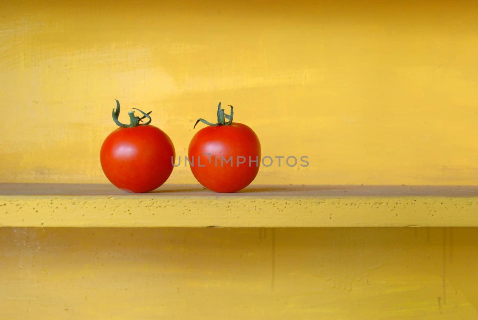 Two red tomatoes in yellow wooden shelf.