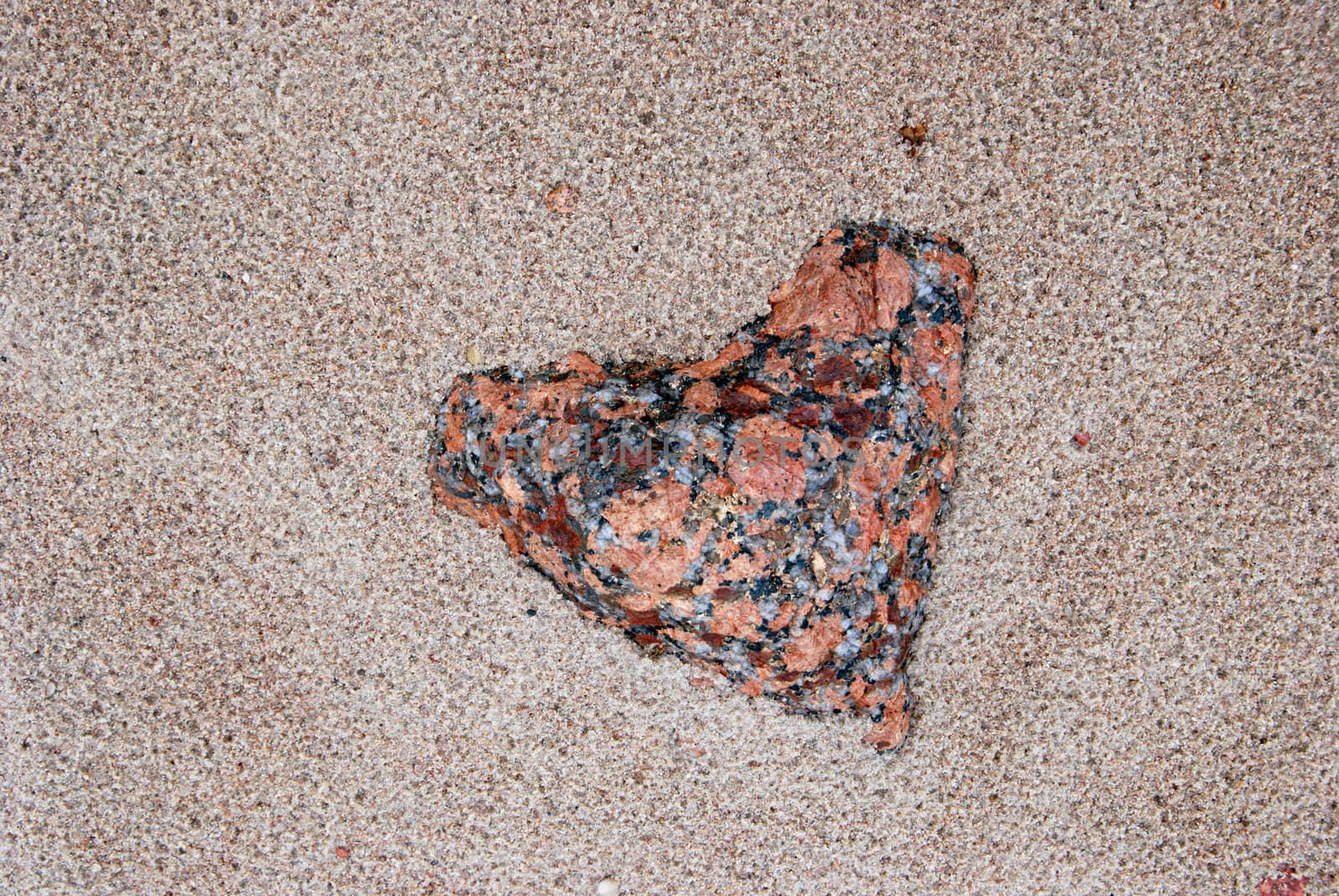 Valentine's stone (hearts form) covered with sand in seashore.