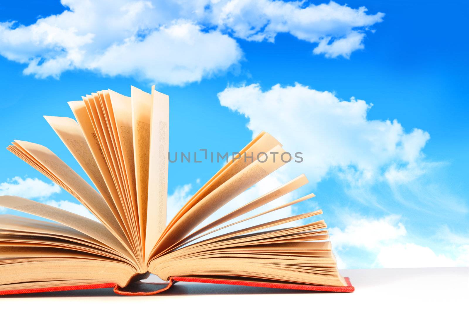 Open book on white surface against a blue sky