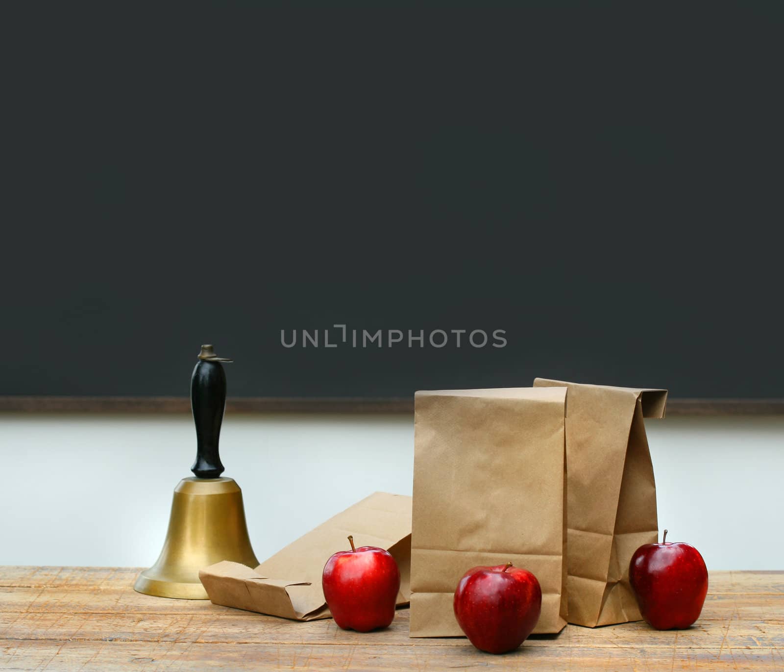 Paper lunch bags with apples and school bell on desk