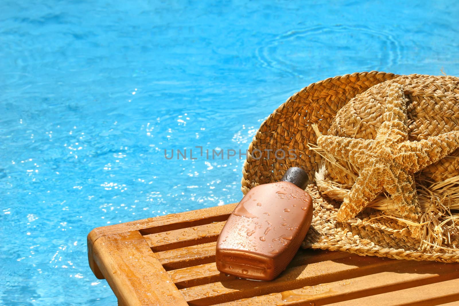 Suntan lotion and straw hat by the pool
