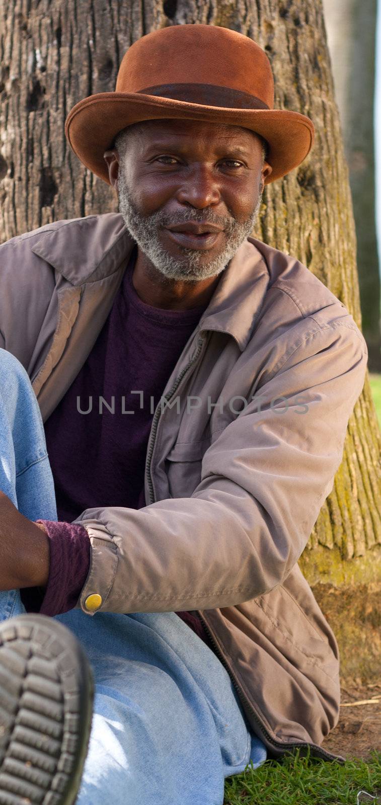 A man sitting back posing a question.  He is rested against a tree.