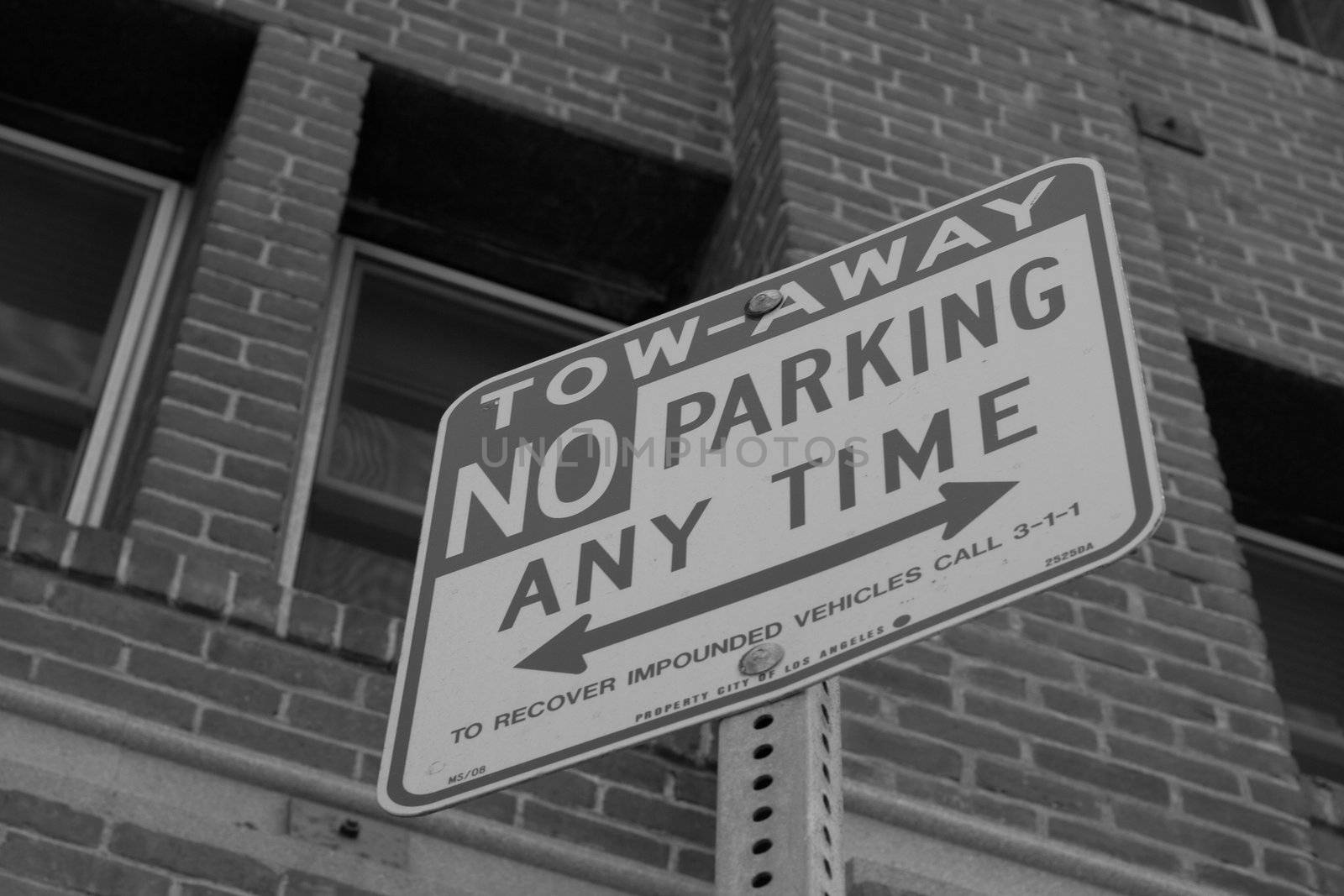 A photograph of a Tow Away No Parking Sign.  The sign has an old brick building in the background.
