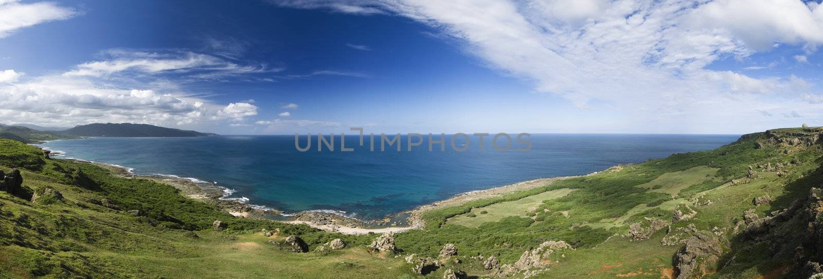 It is a beautiful panoramic coastline with blue sky and green grassland.