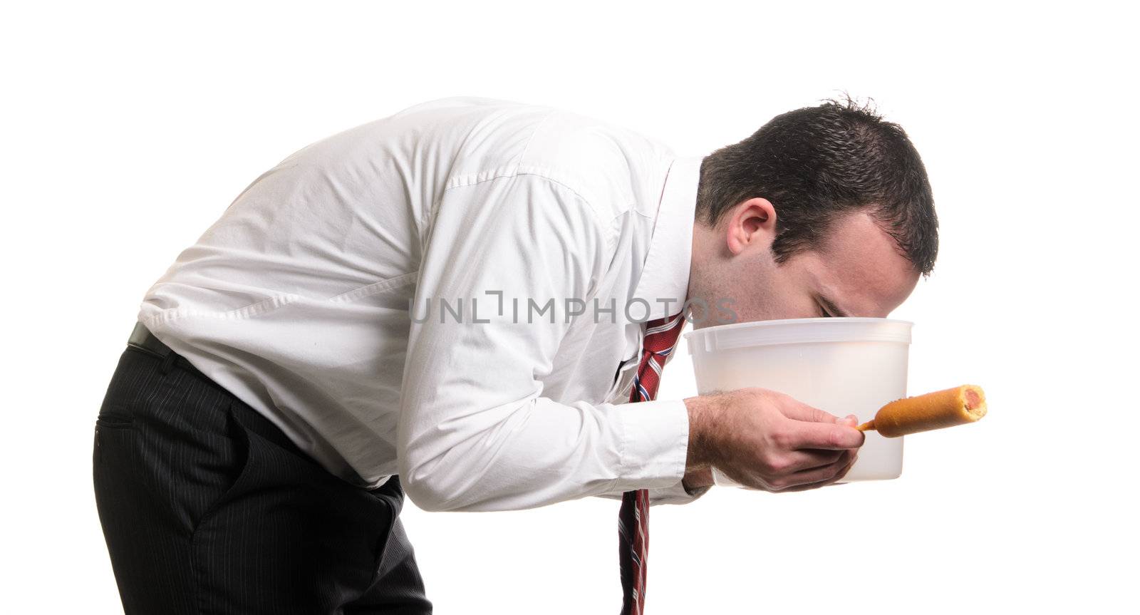 A young man is vomiting into a pail after eating a bad corn dog and getting food poisoning, isolated against a white background.