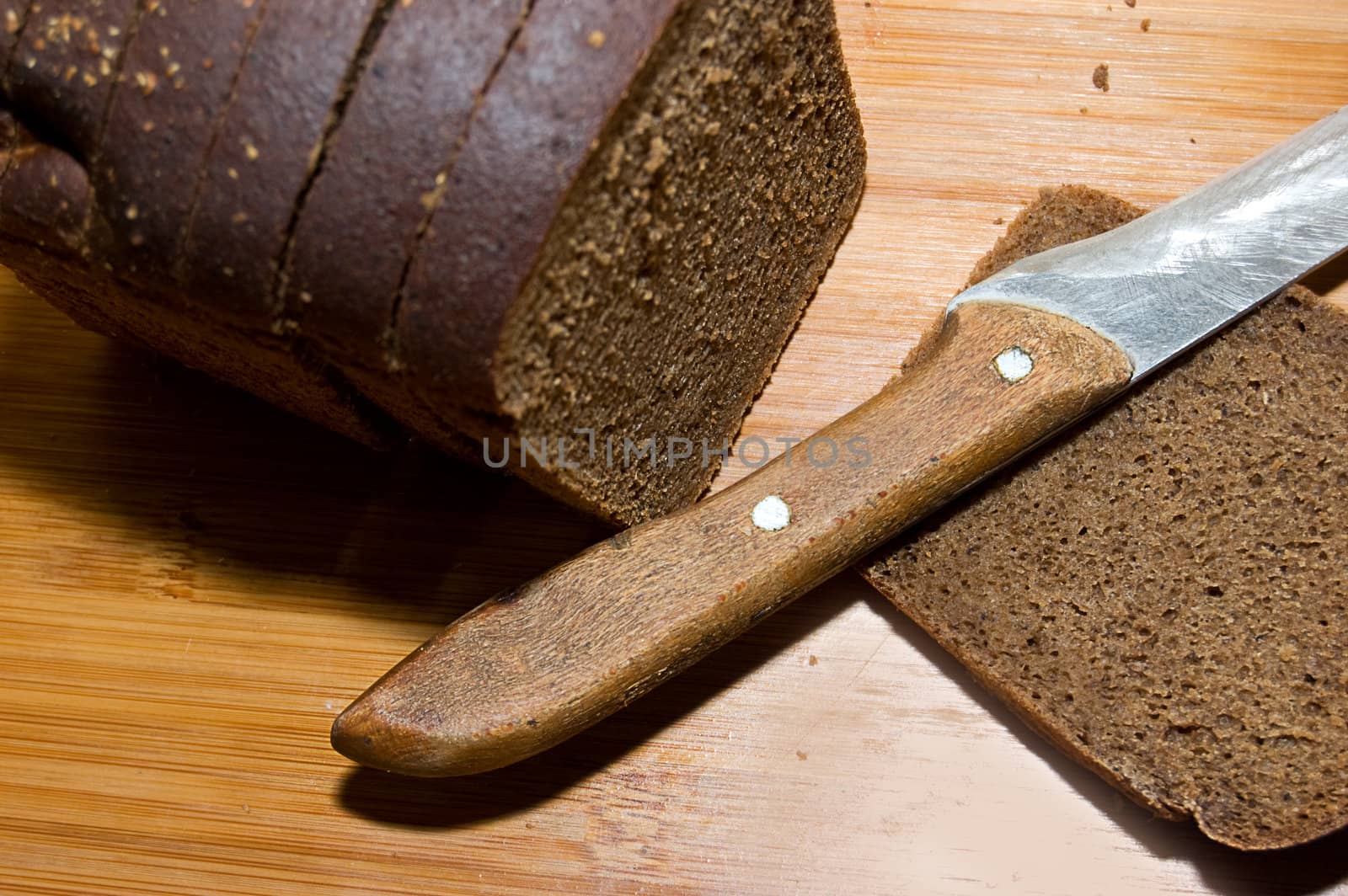Loaf of black bread and knife on wooden board