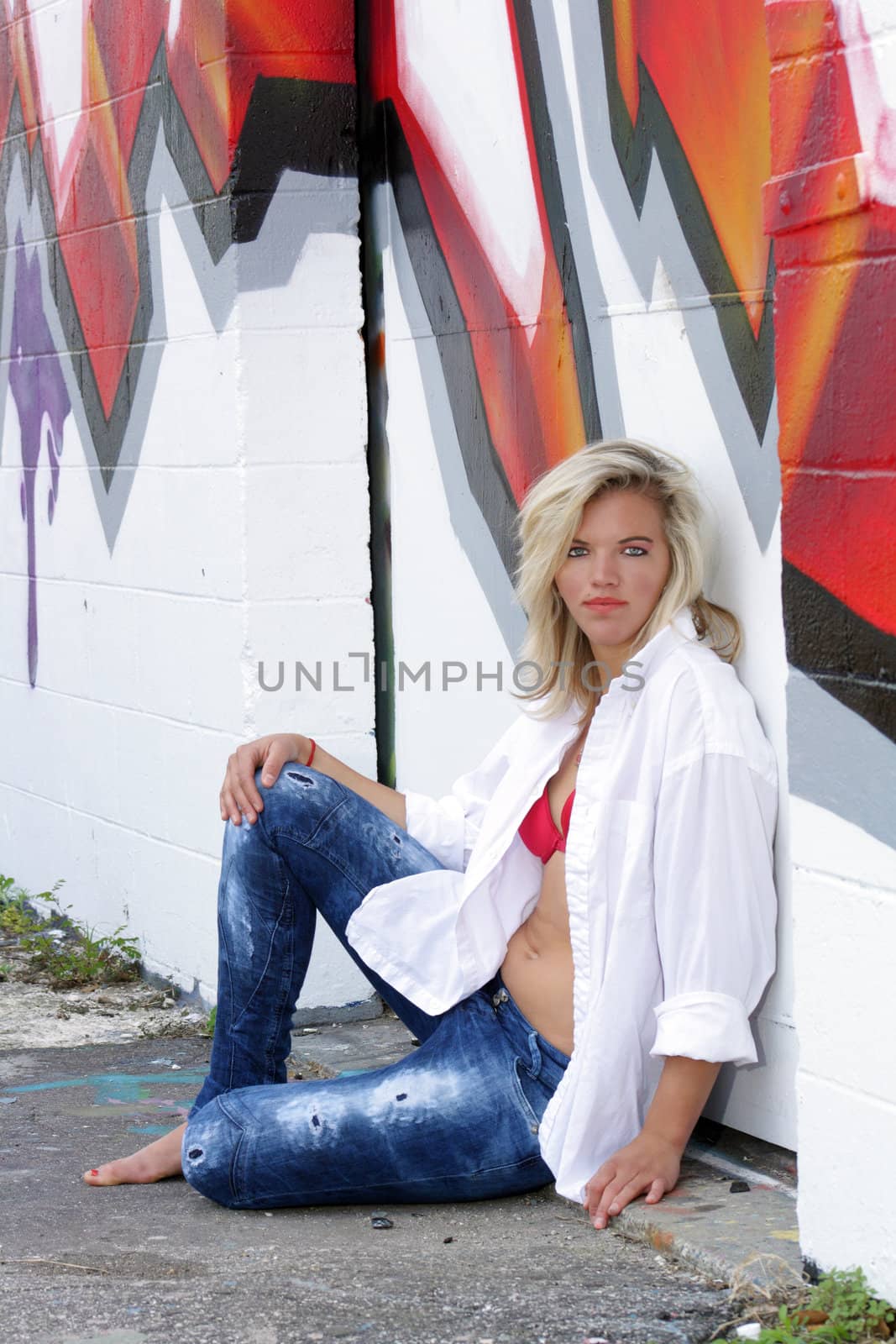 A lovely young blonde leans against a graffiti-covered wall.