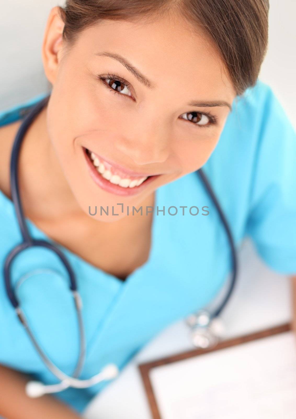 Medical professionals: Woman nurse smiling while working at hospital writing medical report. Young multiracial asian / caucasian female health care worker.