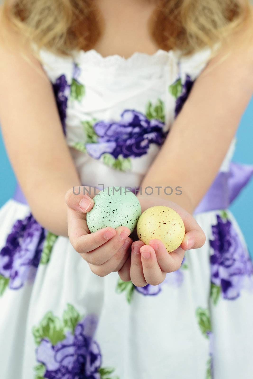 Little girl in her Easter dress holds out two beautifully decorated Easter eggs.