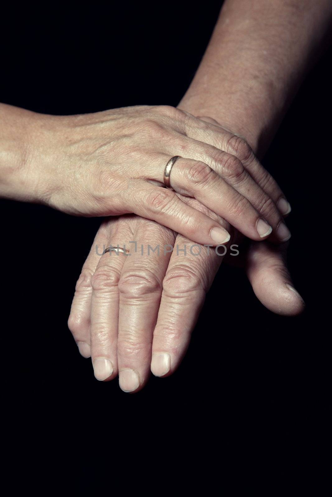 Hands of two loving senior people on a dark background