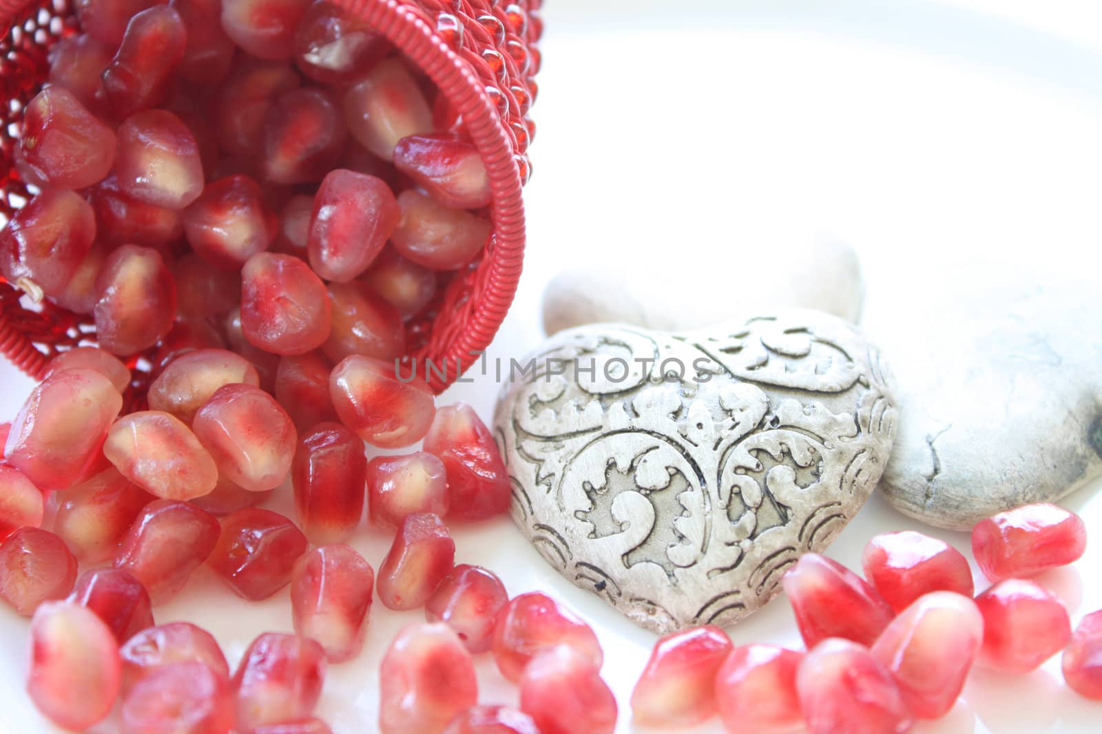 Pomegranite seeds spilling from a decorative container with ceramic hearts