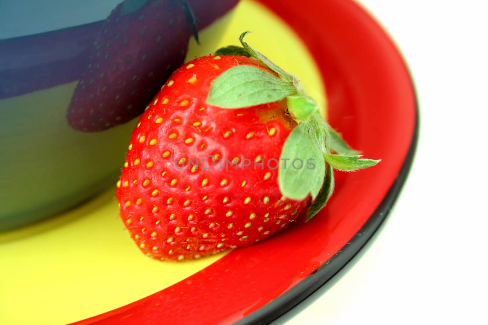 A single strawberry on a colorful coordinated plate isolated on a white background.
