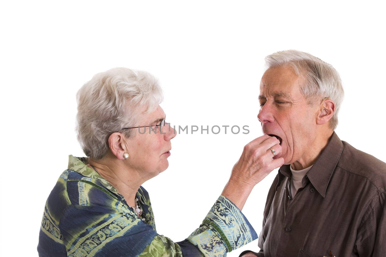 Elderly couple having fun; the woman is putting a chocolate in her husbands mouth