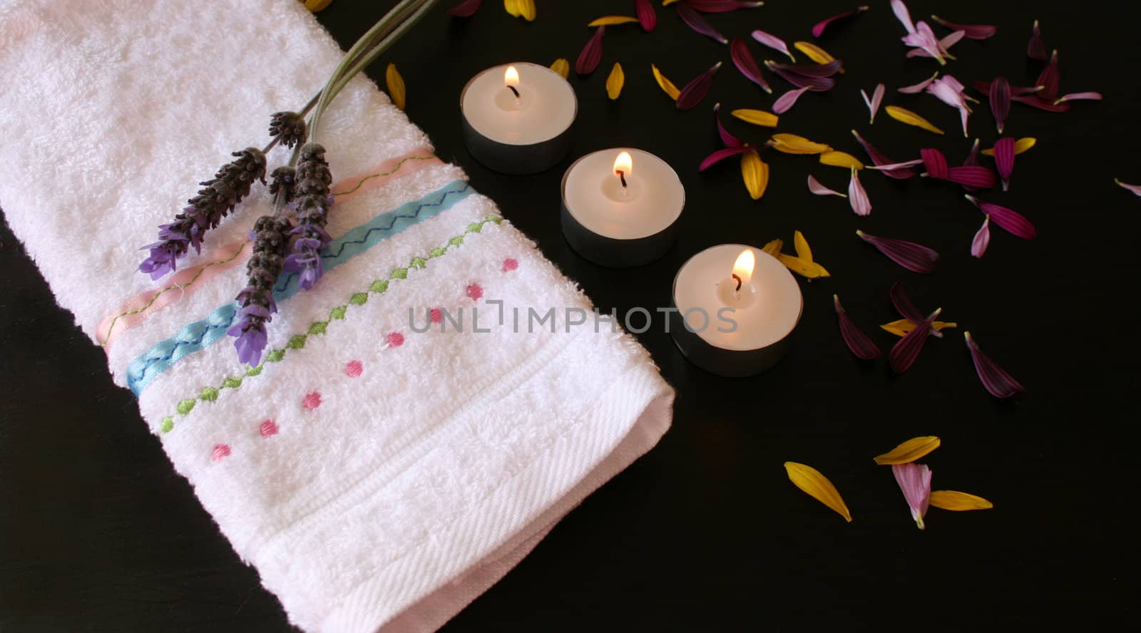 Candles and petals on a brown surface next to a hand towel
