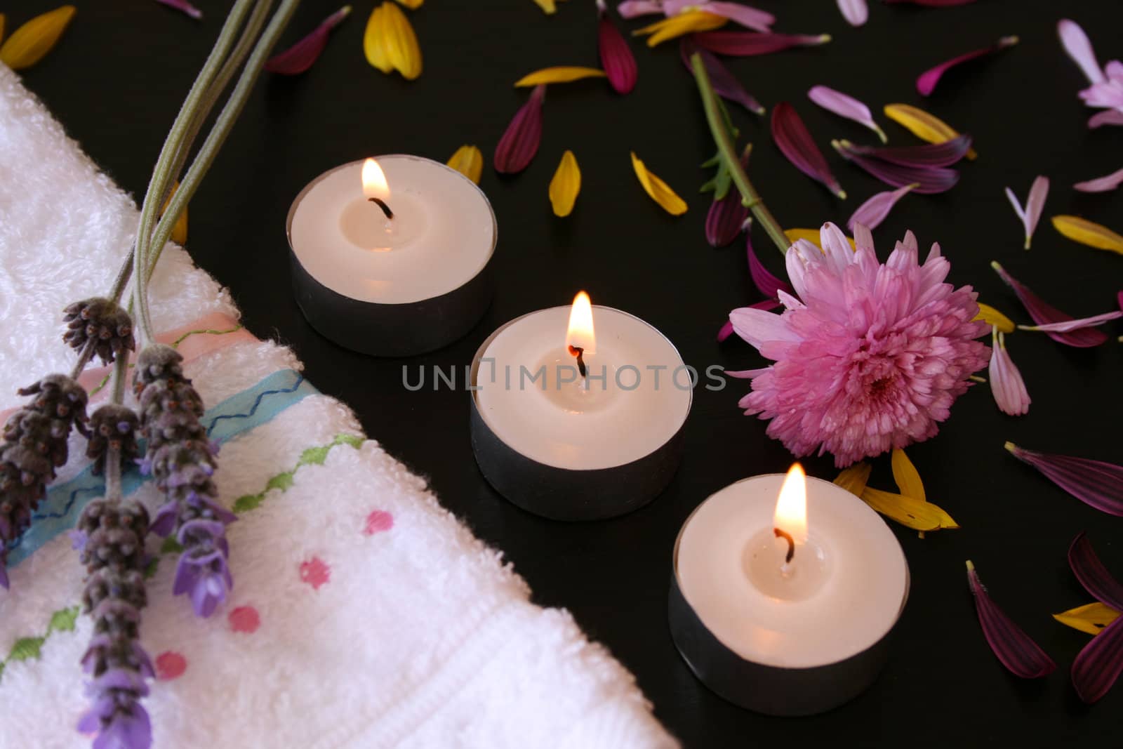 Three teelights next to a hand towel with fresh flowers and petals
