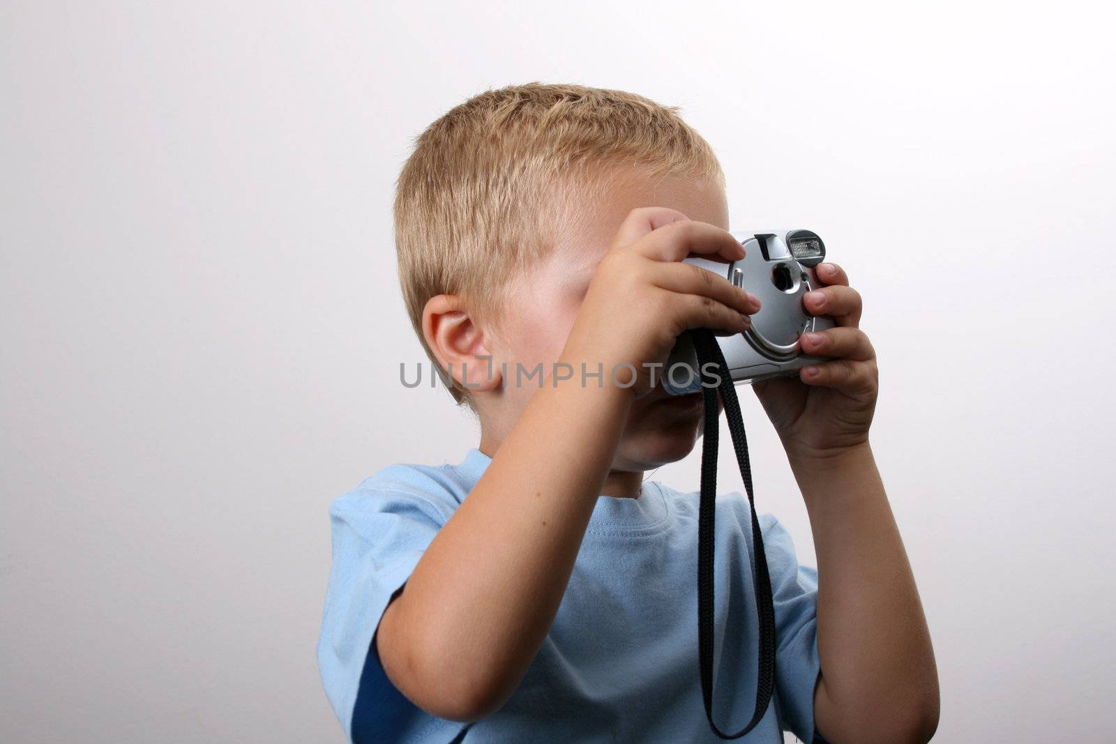 Shy toddler holding a silver camera, looking at his object