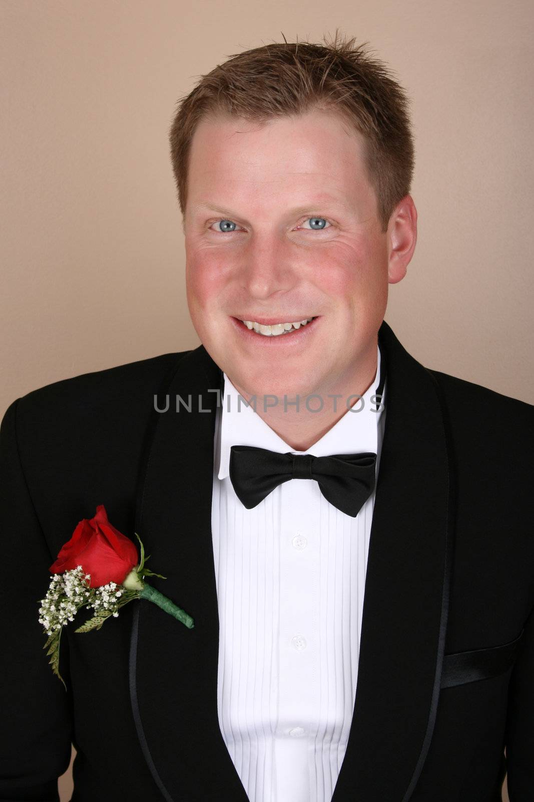 Smiling groom on his wedding day wearing a red rose corsage