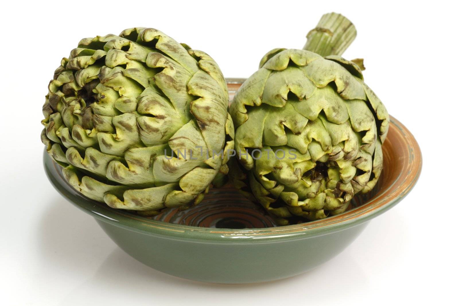 Two fresh artichokes in a bowl over white background