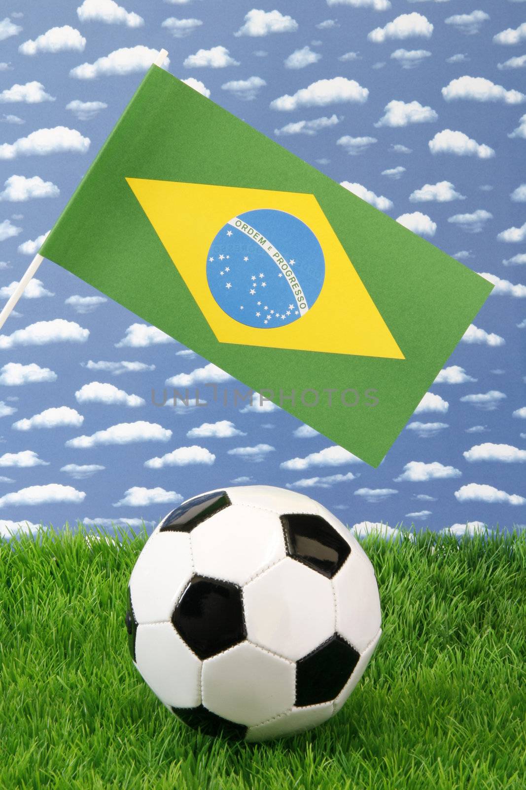 Soccerball on grass with brazilian national flag over sky background