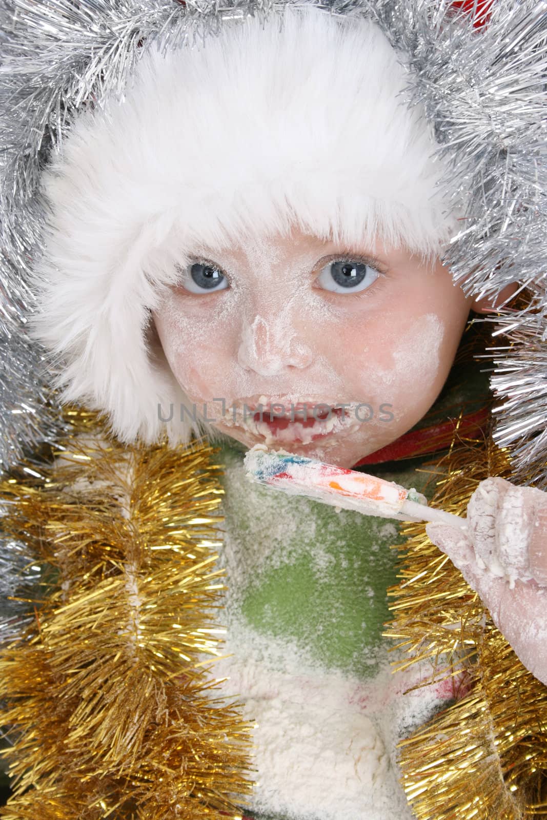 Toddler covered with christmas decorations after baking, eating a lollie