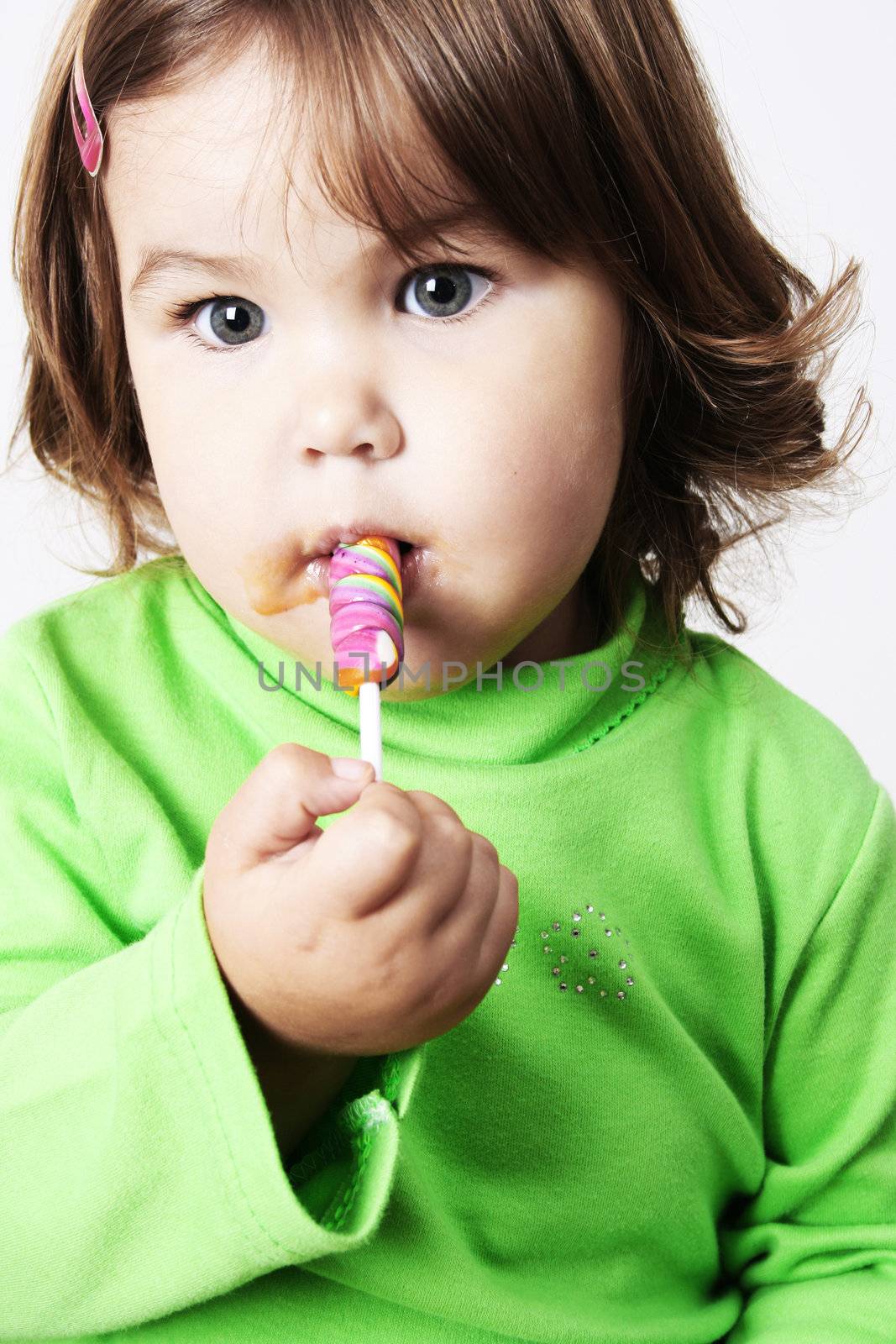 Toddler girl with chubby cheeks eating a sticky lollipop
