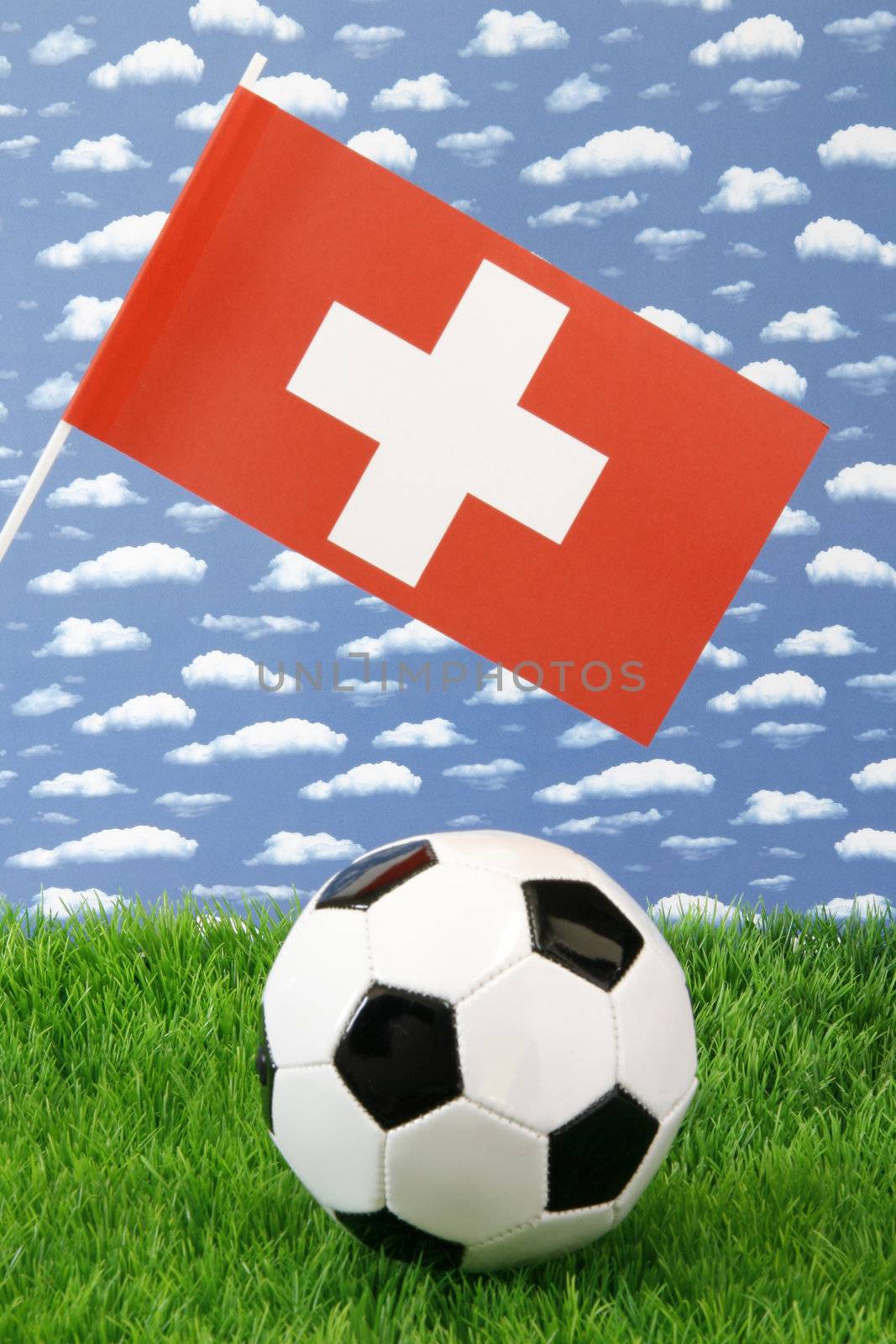 Soccerball on grass with swiss national flag over sky background