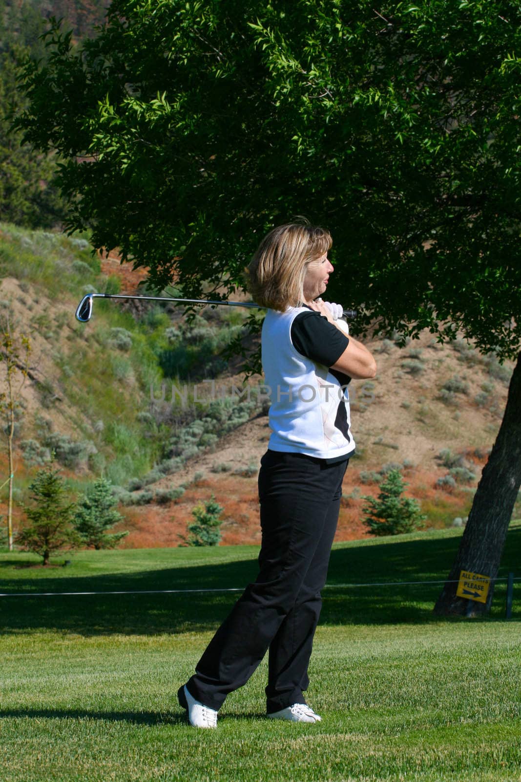 Blond female golfer following her ball down the fairway