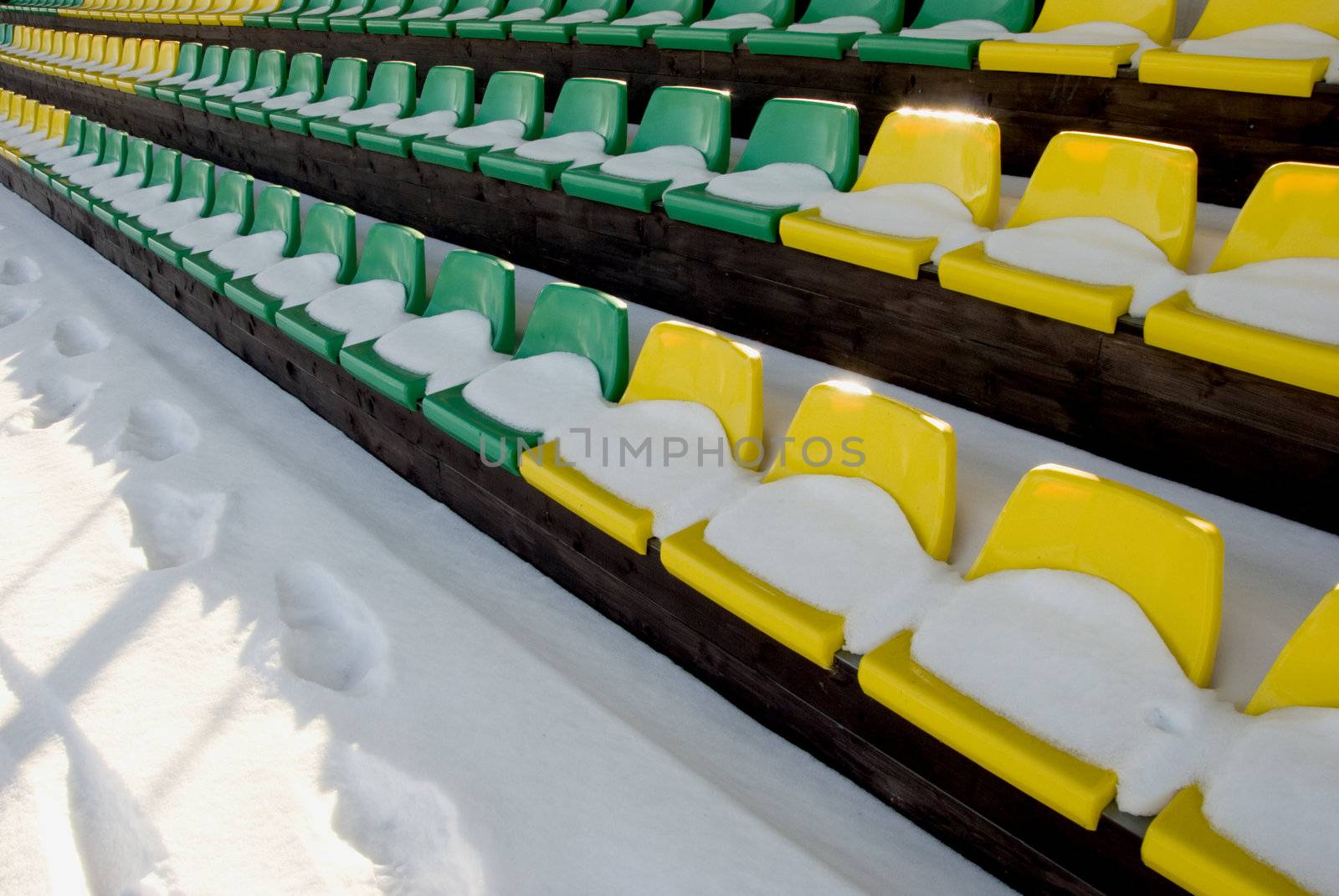 football stadium tribune yelow and green chairs with winter snow