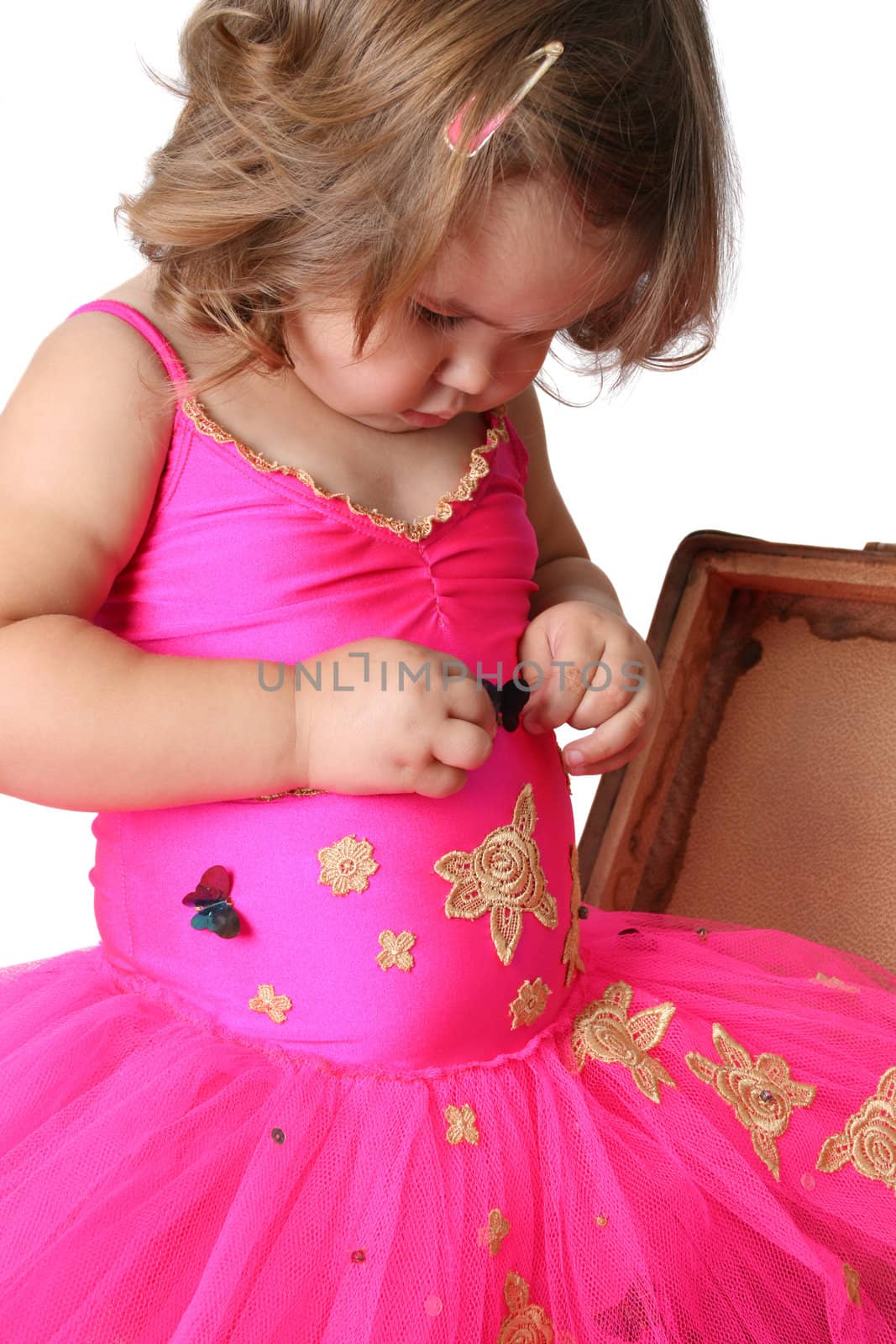 Little girl with wearing a bright pink tutu standing in an old suitcase
