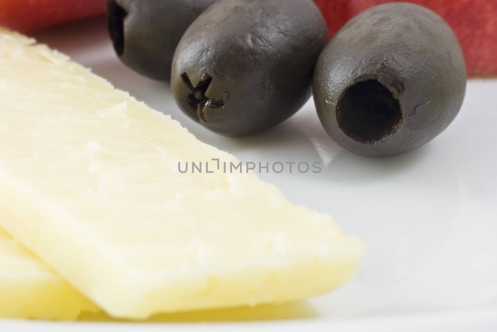 Macro shot of cheddar cheese and olives on a white plate.  Red apple just visible in the background.